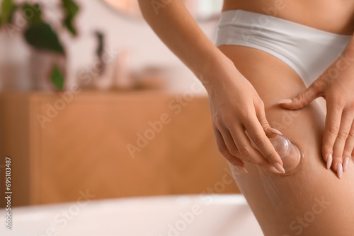 Young woman massaging her thigh with anti-cellulite cup in bathroom, closeup photo