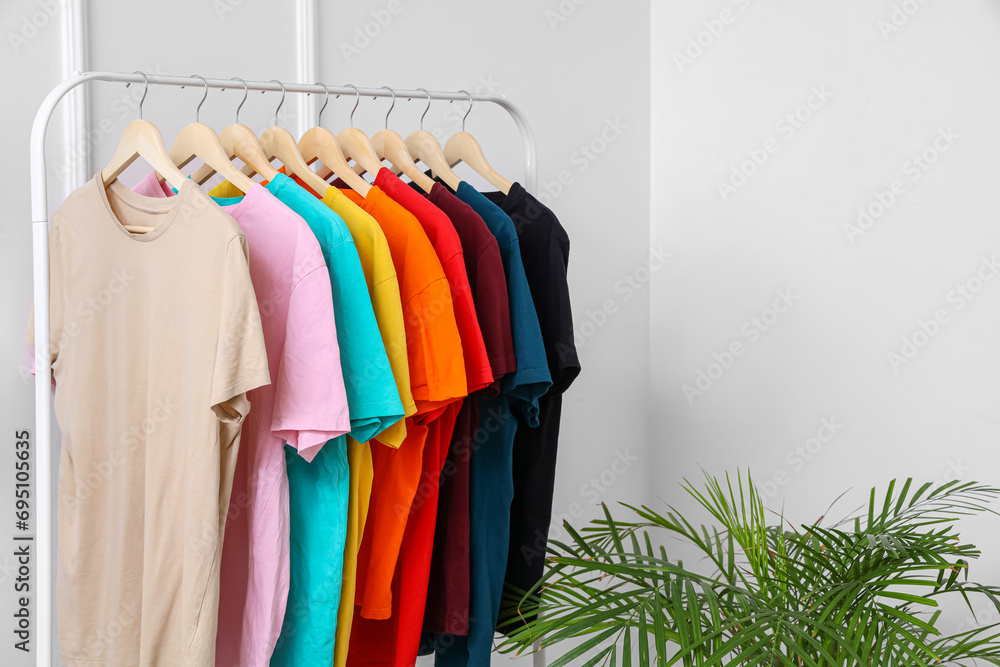 Obraz premium Rack with colorful t-shirts near light wall