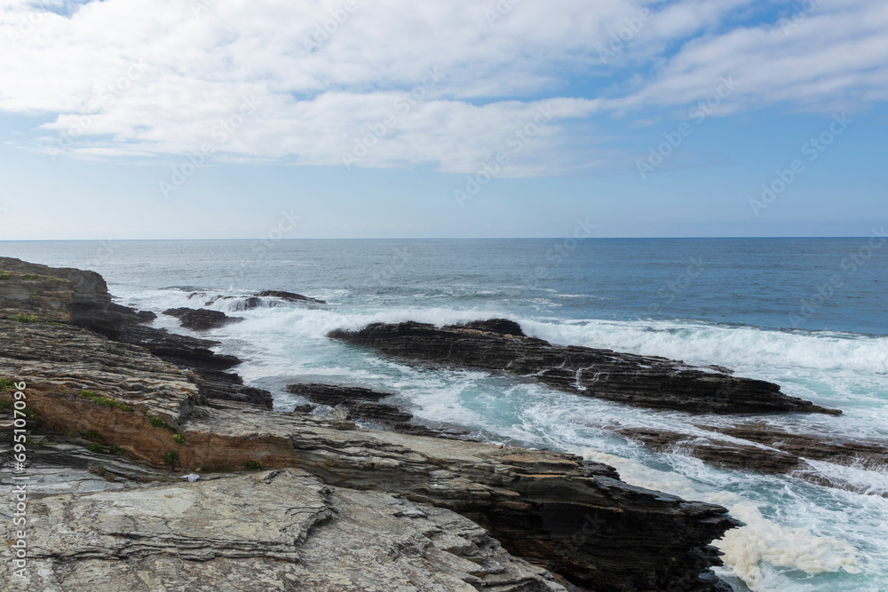 Waves crash on a rocky coast under a partly cloudy sky, capturing nature s serene and rugged beauty Waves crash on a rocky coast under a partly cloudy sky, capturing nature s serene and rugged beauty