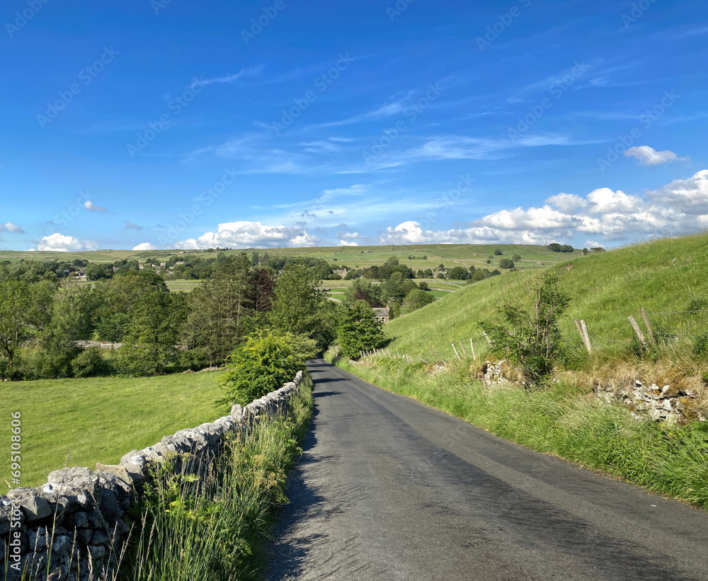 View down, Church Road, with dry stone walls, fields and hills near the Yorkshire Dales village of, Linton, UK