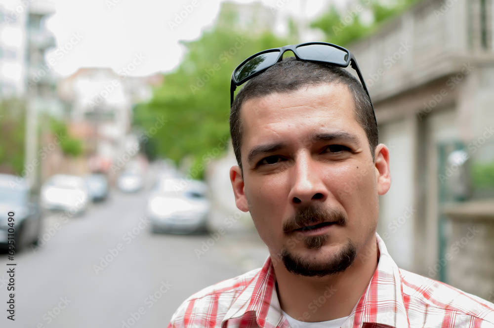 Portrait of handsome man with beard and sunglasses in plaid red and white in the city street Portrait of handsome man with beard and sunglasses in plaid red and white in the city street