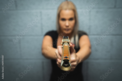 A blonde girl takes aim from a golden Desert Eagle pistol, soft focus photo. photo