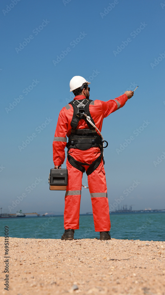 Engineer with orange safety uniform and safety harness work at site line of factory