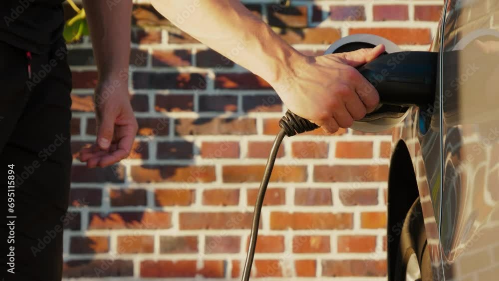 Male hand unplug power connector from EV car, closeup. Unrecognizable