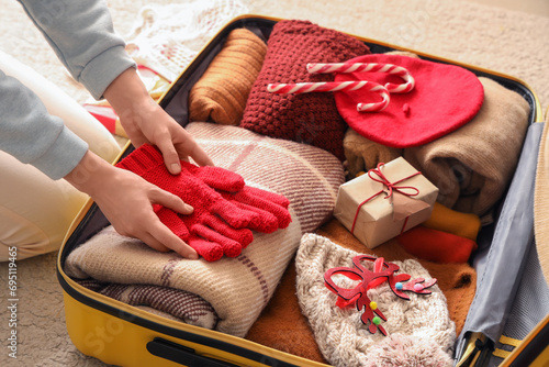 Woman packing clothes, Christmas gift and decor into suitcase, closeup photo
