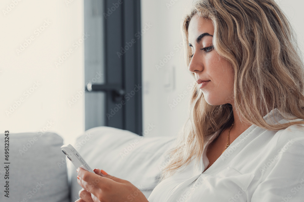 Portrait of one young attractive blonde woman using phone cell on couch relaxing surfing the net at home. Relaxing online concept lifestyle.