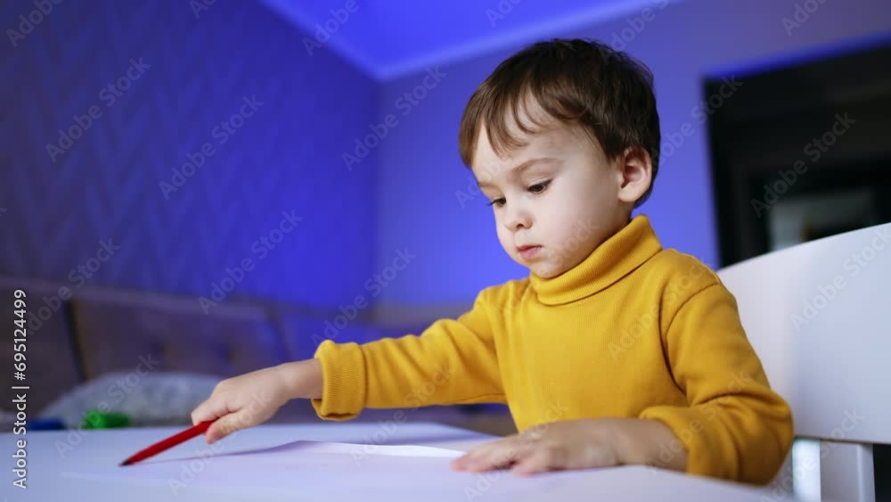 Serious toddler boy sitting at desk drawing with felt-pen. Infant child puts the pen and stands up. Serious toddler boy sitting at desk drawing with felt-pen. Infant child puts the pen and stands up.