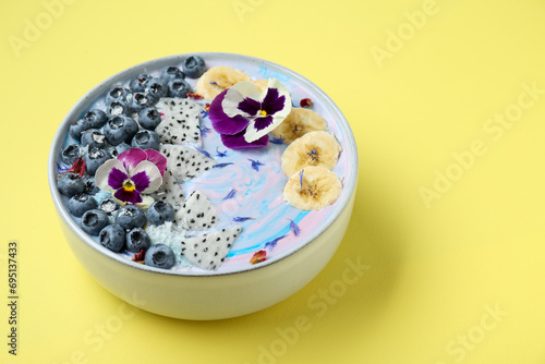 Delicious smoothie bowl with fresh fruits, blueberries and flowers on yellow background, closeup. Space for text