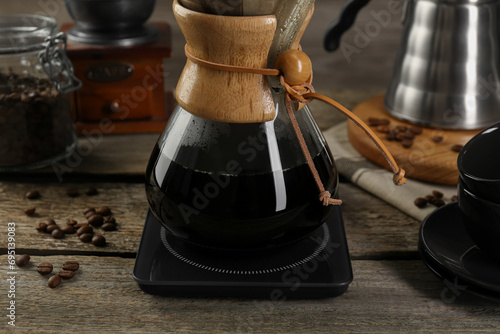 Glass chemex coffeemaker with coffee and beans on wooden table, closeup photo
