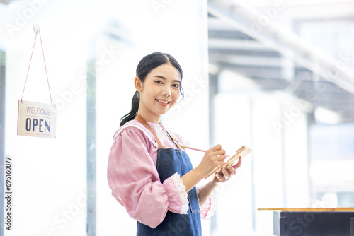 Portrait of happy waitress standing at restaurant entrance. SME entrepreneur young business asian woman attend new customers near door. Smiling small business owner showing open sign in her shop.