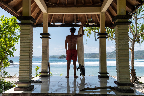 Surfer contemplating the waves from beachside pavilion, Indonesia, Asia photo