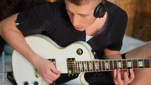 Young man in headphones yank strings of electric guitar photo
