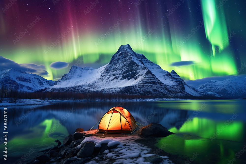 Tent with light at night, with northern lights over snowy mountain and lake