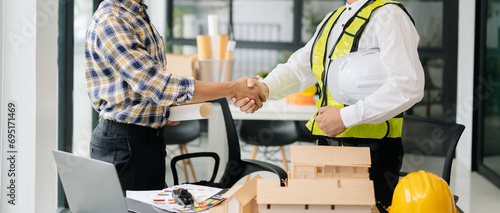 Construction team shake hands greeting start new project plan behind yellow helmet on desk in office photo