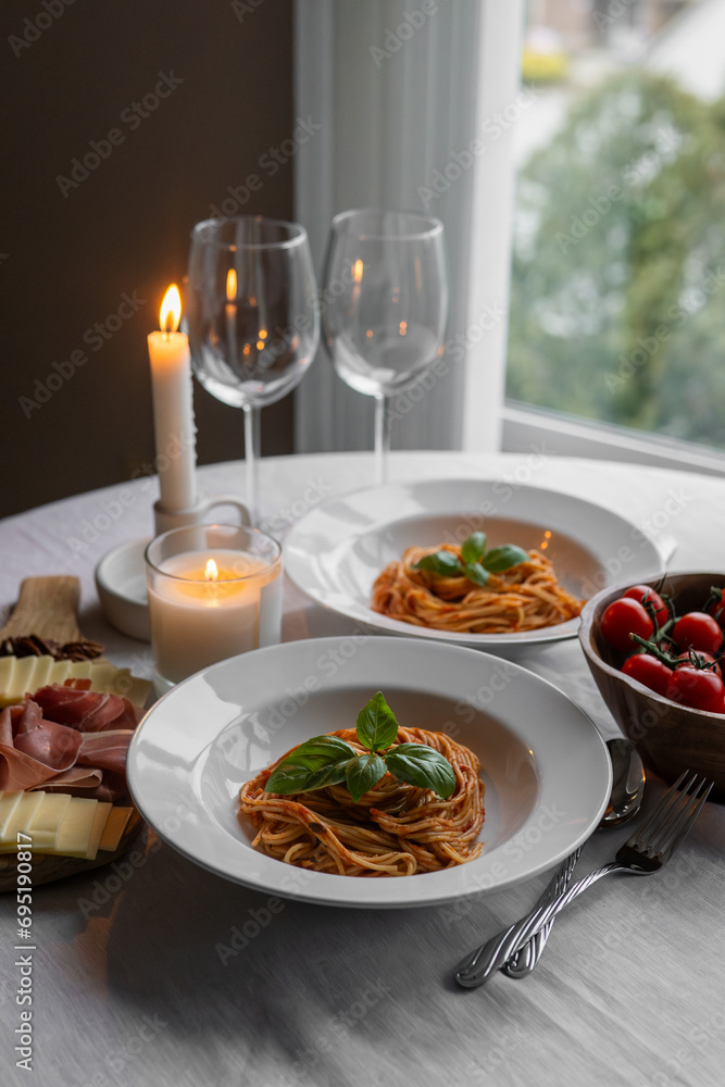 Savory bolognese pasta with basil, prosciutto, cheese, and nuts. A table set with сherry tomatoes, candles, and wine glasses completes a rustic table.