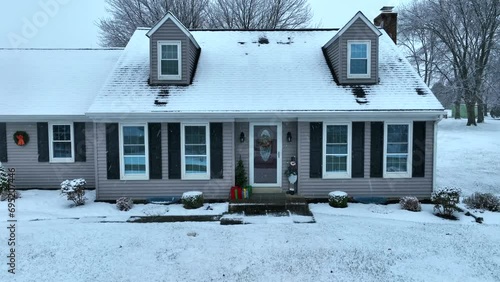 House with snowy roof and holiday decorations during Christmas time. Aerial push in with snow flurries. photo
