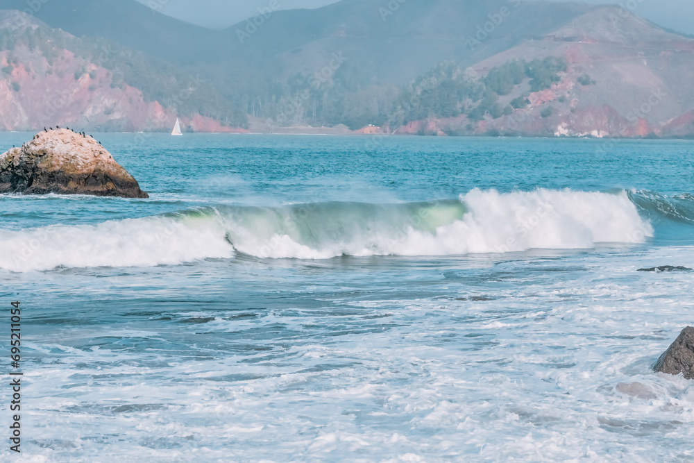 Fototapeta premium Wave splashes close-up. Crystal clear sea water hitting rock formations in the ocean in San Francisco Bay, blue water, pastel colors.