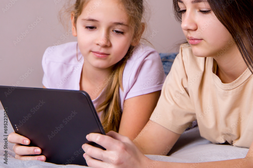 Two teen girls lying on bed and using digital tablet. Selective focus. Two teen girls lying on bed and using digital tablet. Selective focus.