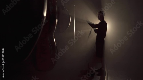 Silhouette of young boxer winds boxing bandages before a match, fight or training. Light in the dark gym. photo