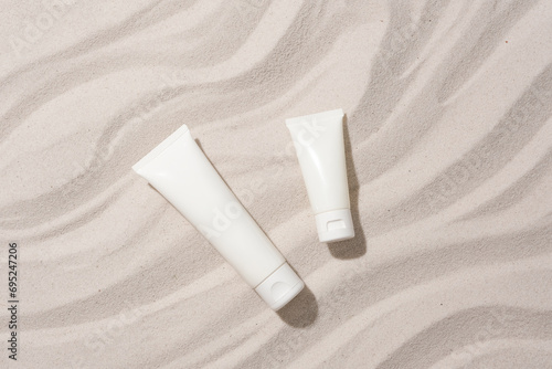 Close-up of two unlabeled cosmetic tubes placed on a sandy background with wave patterns. Mockup for cosmetics advertisement with blank label. photo