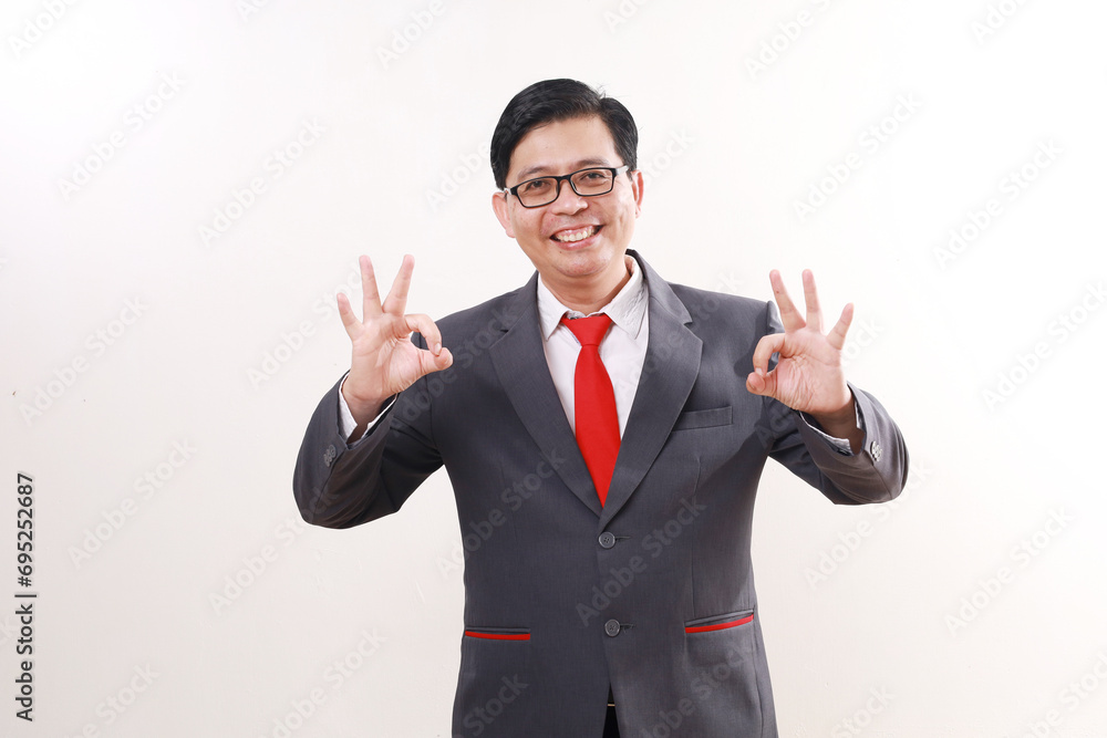 Excited satisfied asian businessman standing while showing okay hand gesture. Isolated on white Excited satisfied asian businessman standing while showing okay hand gesture. Isolated on white