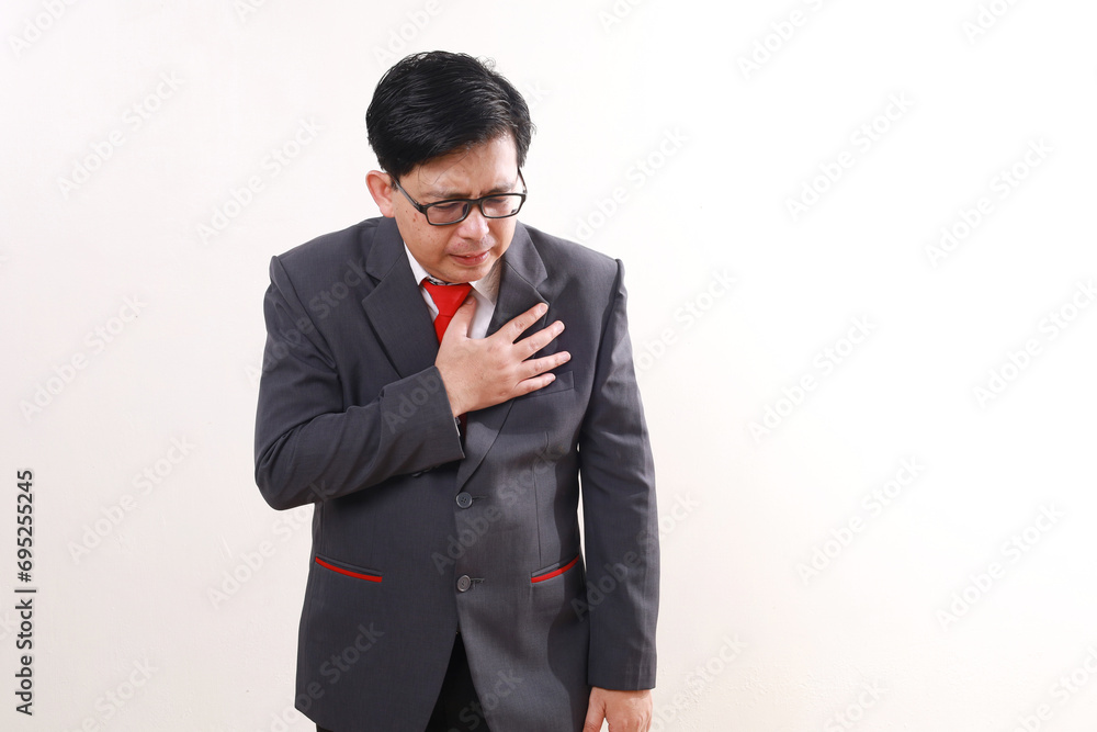 Asian businessman standing while holding chest. He suffering from chest pain. Heart attack concept Asian businessman standing while holding chest. He suffering from chest pain. Heart attack concept