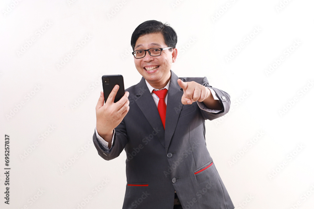 Excited asian businessman holding a cell phone white pointing at you. Isolated on white Excited asian businessman holding a cell phone white pointing at you. Isolated on white