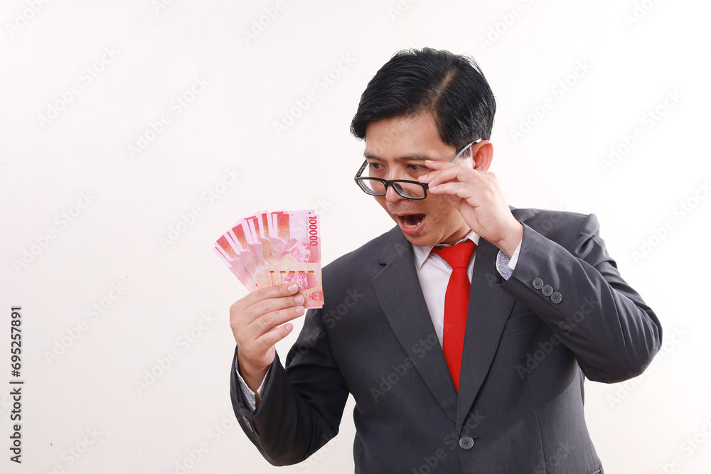 Wow excited asian businessman standing while holding Indonesia banknotes. Isolated on white Wow excited asian businessman standing while holding Indonesia banknotes. Isolated on white