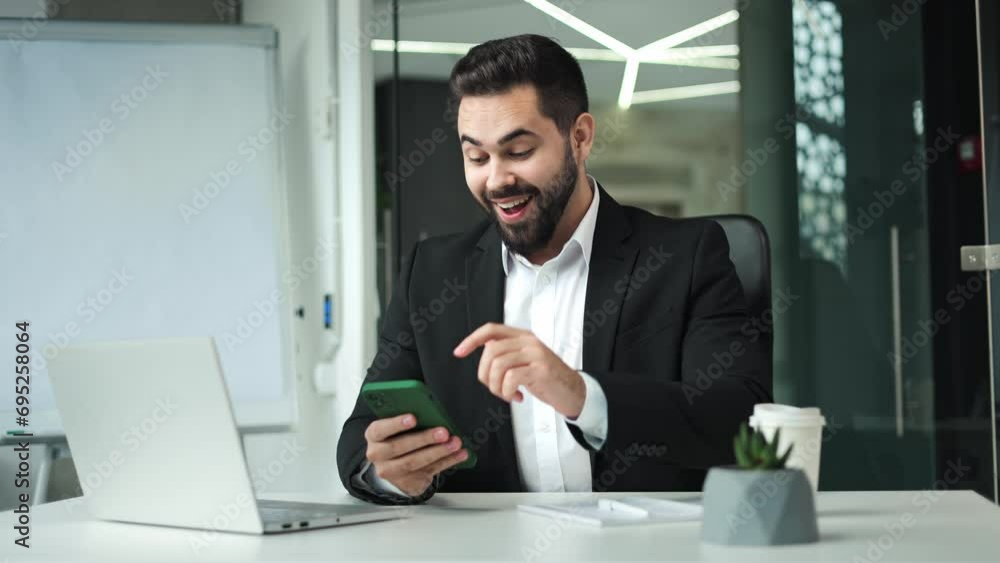 Happy man expressing sincere happiness and gesturing while enjoying result of own project. Successful businessman using personal smartphone to monitoring work process while sitting at office. Happy man expressing sincere happiness and gesturing while enjoying result of own project. Successful businessman using personal smartphone to monitoring work process while sitting at office.