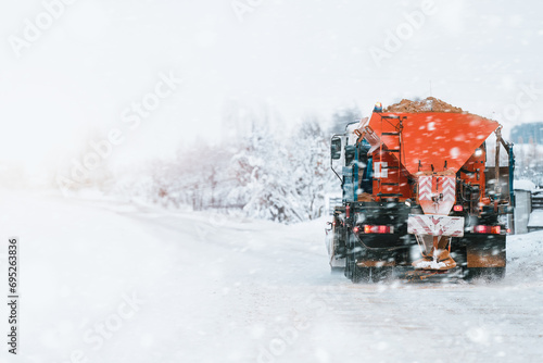 Tractor with mounted salt and sand spreader, road maintenance - winter gritter vehicle. Municipal service melting ice and snow on streets. Diffusing salt blend on public roads.