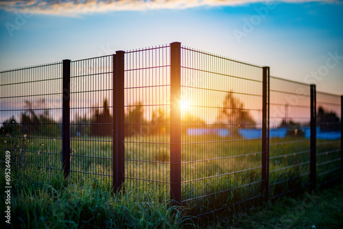  Sunset casts golden light over fence, field, and distant landscape.