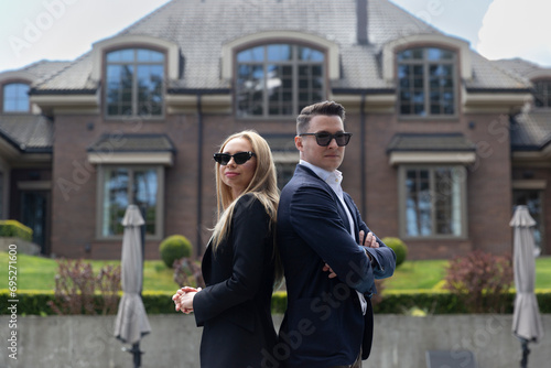Successful and rich couple buying new residence at estate management company. Woman and man in formal suits against summer cottage