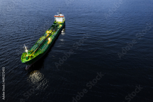Small illuminated tanker ship with green deck in the dark blue ocean water. Aerial view. Oil and gas transportation and supply. High value goods delivery by water. Logistics and marine trade. © mark_gusev