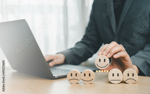 The client's hand picked the happy face smile face icon and five star symbol on wooden cube on table. Customer service evaluation and satisfaction survey concepts.