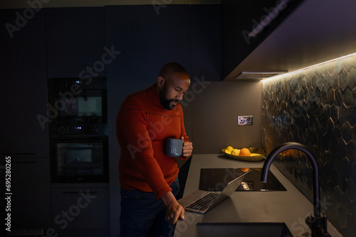 Man working on laptop late at night at home in kitchen photo