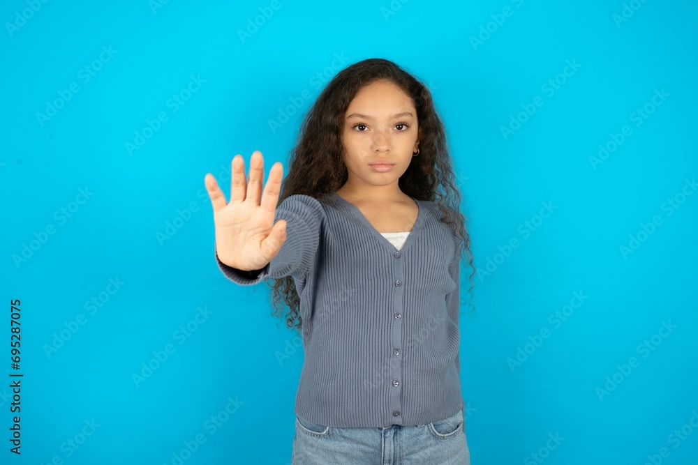 Beautiful teen girl wearing blue jacket over blue background doing stop sing with palm of the hand. Warning expression with negative and serious gesture on the face. Beautiful teen girl wearing blue jacket over blue background doing stop sing with palm of the hand. Warning expression with negative and serious gesture on the face.