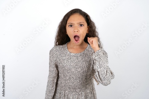 beautiful caucasian teen girl wearing flowered dress angry and mad raising fist frustrated and furious while shouting with anger. Rage and aggressive concept.