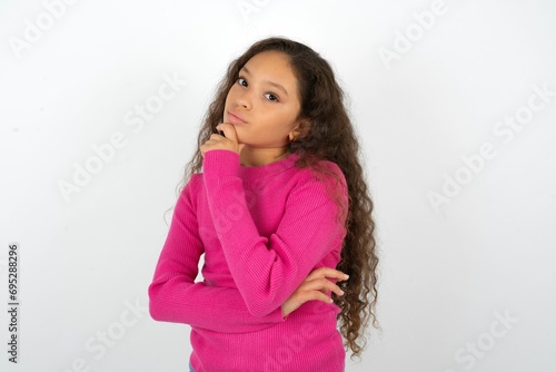 Beautiful teen girl wearing pink sweater over white background looking confident at the camera smiling with crossed arms and hand raised on chin. Thinking positive. © Roquillo