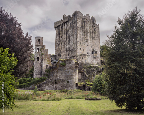 medieval stone castle stronghold  is partial ruin near Cork Ireland with a beautiful garden in the foreground and a bright cloudy sky in the background