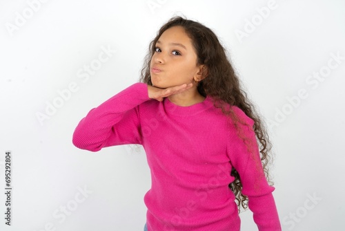 Beautiful teen girl wearing pink sweater over white background cutting throat with hand as knife, threaten aggression with furious violence.