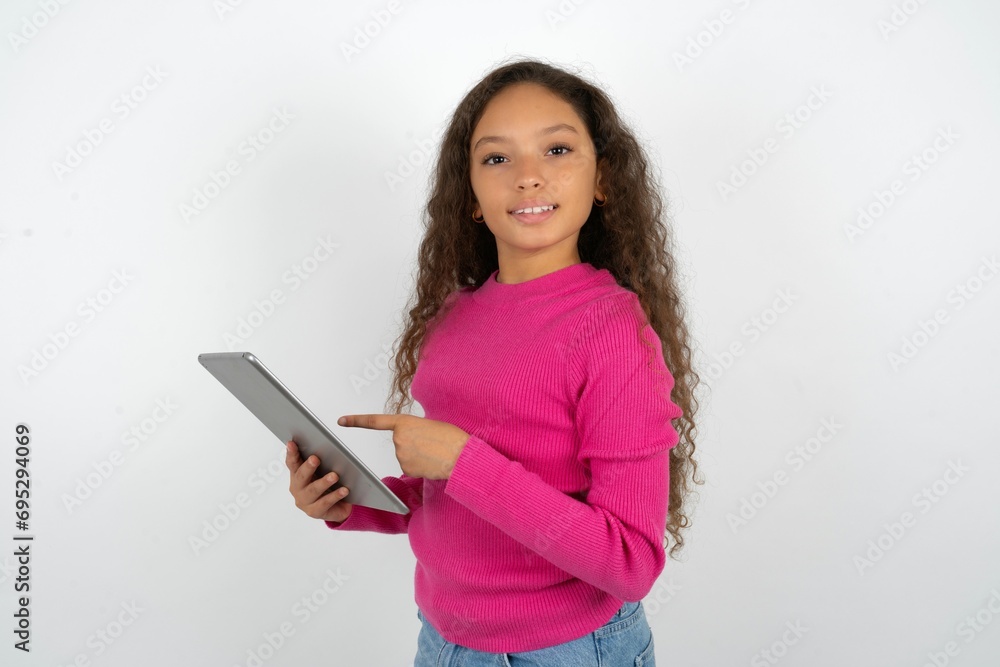 Photo of happy cheerful smart Beautiful teen girl wearing pink sweater over white background hold tablet browsing internet Photo of happy cheerful smart Beautiful teen girl wearing pink sweater over white background hold tablet browsing internet