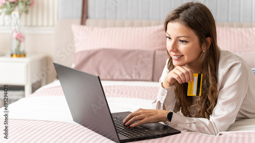 Happy young beautiful woman holding credit card and using laptop making payment online at home. Online shopping, e-commerce, banking, internet store, sale, online purchase, delivery, promotion
