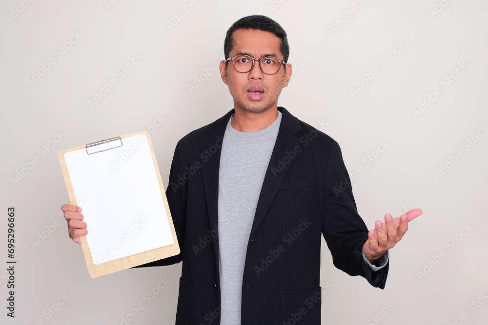Asian businessman showing confuse expression while holding blank white paper on clipboard Asian businessman showing confuse expression while holding blank white paper on clipboard