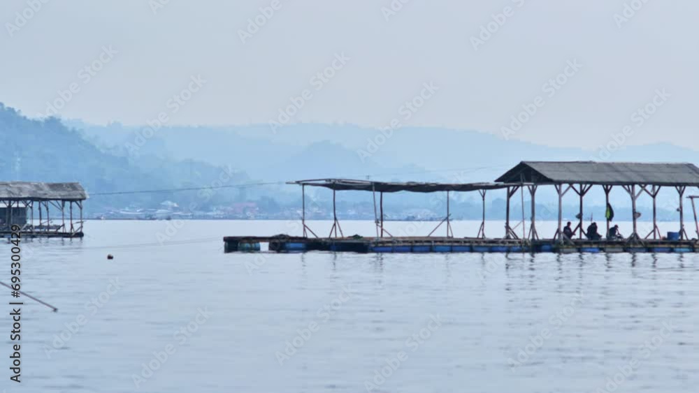 People fishing in floating cages on the calm sea in Lampung with fishing villages in the distance on a misty day People fishing in floating cages on the calm sea in Lampung with fishing villages in the distance on a misty day