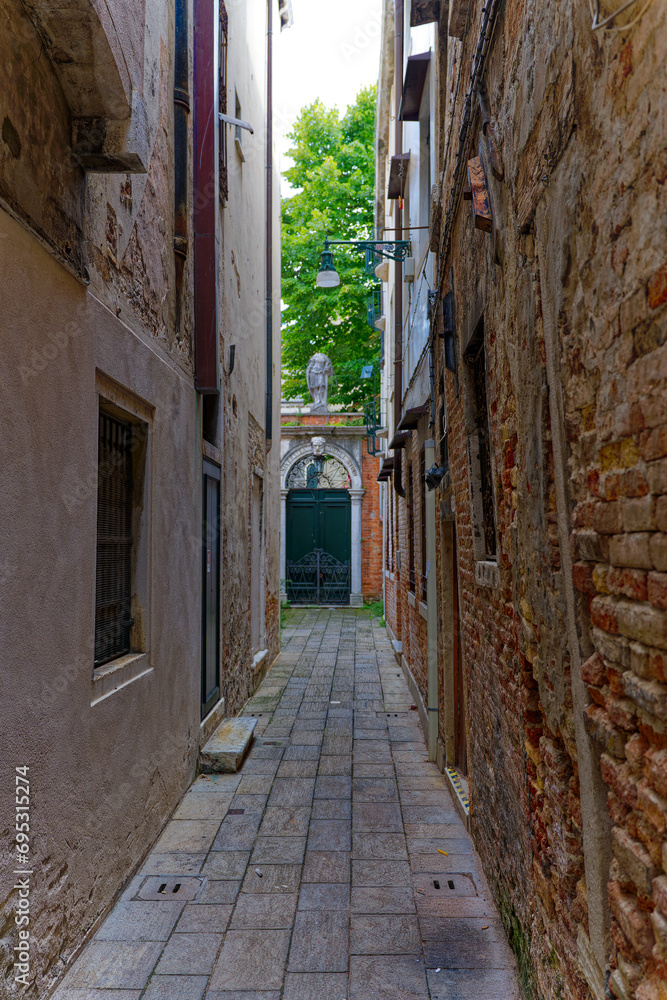 Diminishing perspective of narrow alley at the old town of Venice with facades of historic houses on a sunny summer day. Photo taken August 6th, 2023, Venice, Italy.