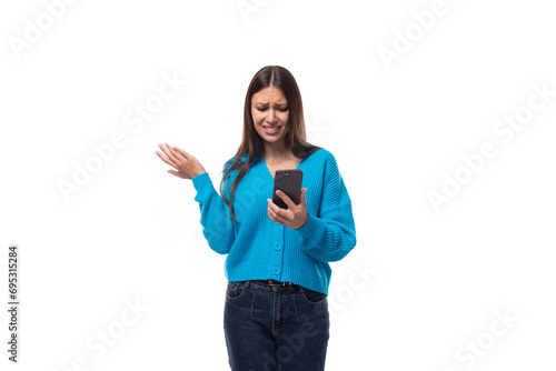 charming caucasian woman with black hair dressed in a blue cardigan reads a message on a smartphone