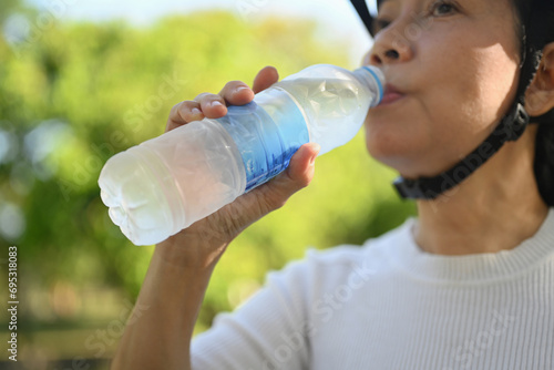 Senior fitness woman drinking water from a bottle resting after riding bicycle in park.