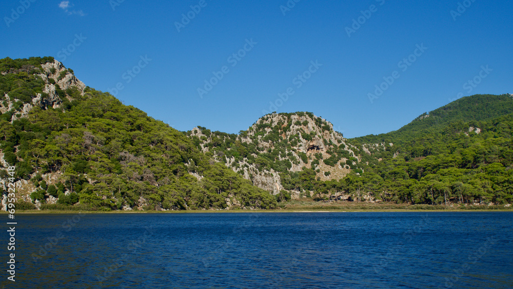 Köyceğiz lake in Muğla, Western Türkiye. Forested and rocky mountains and blue lake. Nature landscape in front of blue sky.