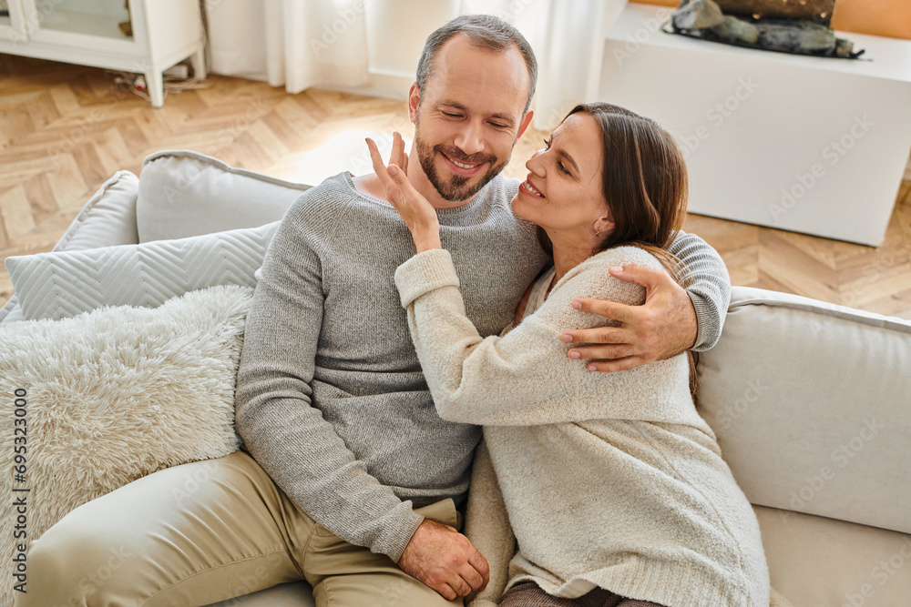 joyful woman embracing happy husband on cozy couch in living room, leisure of child-free couple