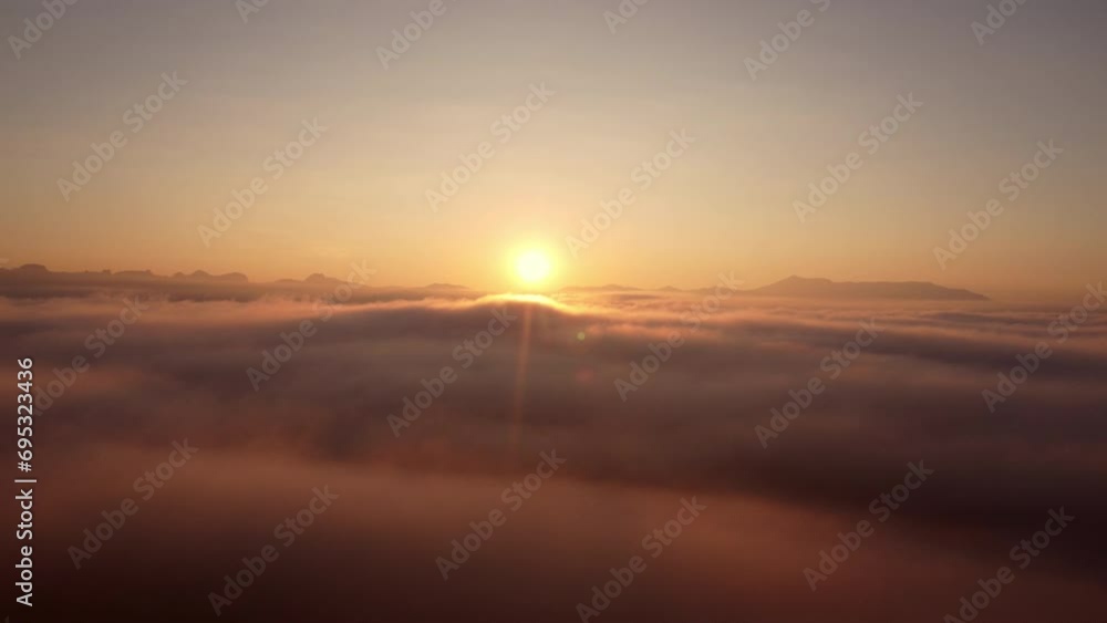 Drone camera flying over thick fog above the beautiful ocean of clouds at sunrise. The sun is rising above the endless sea of clouds until the horizon. Drone camera flying over thick fog above the beautiful ocean of clouds at sunrise. The sun is rising above the endless sea of clouds until the horizon.